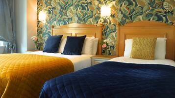 Two beds with headboards, a floral wallpaper, and a nightstand with a lamp.