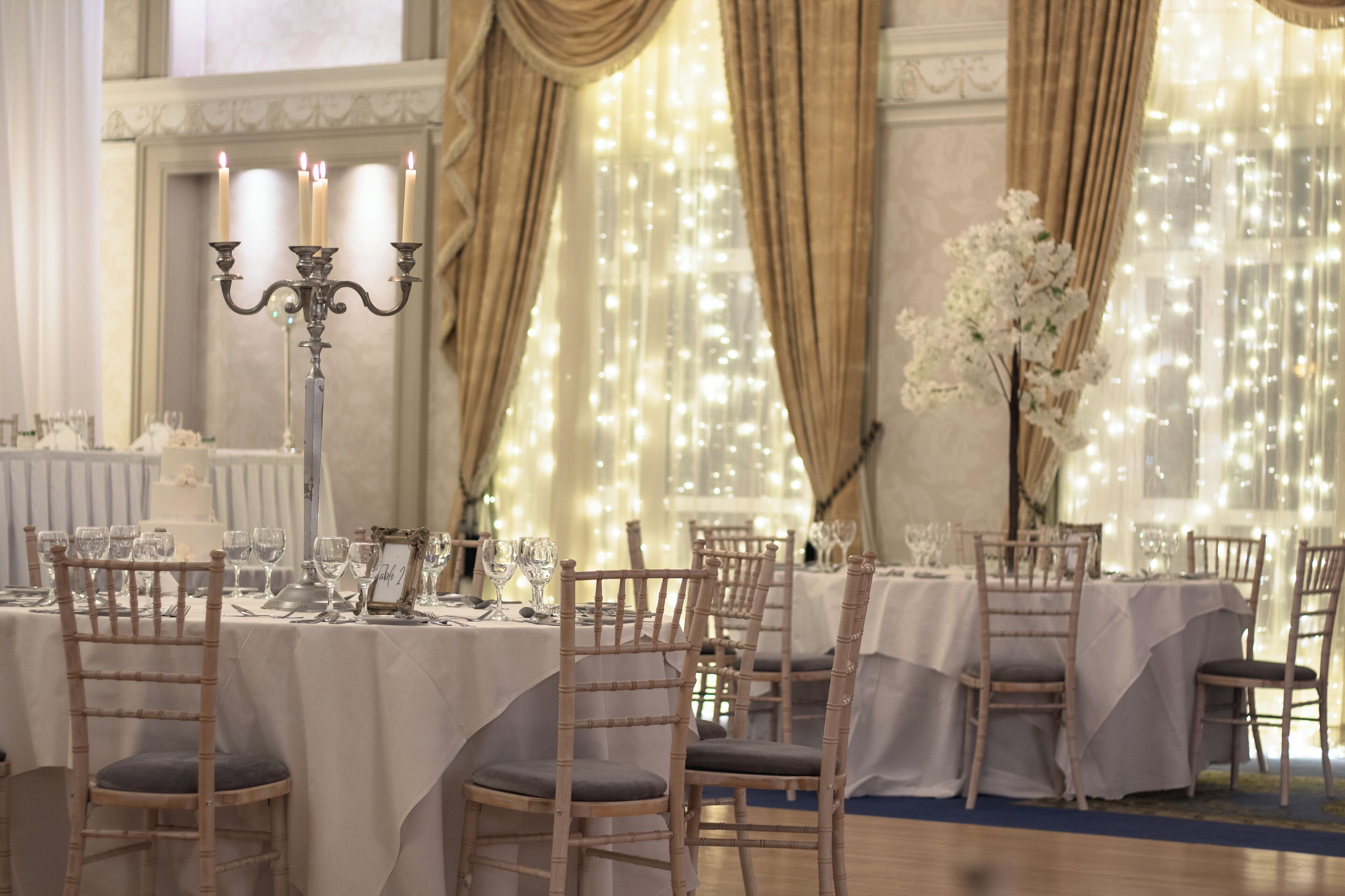 Een feestzaal met gedekte tafels, witte tafelkleden en houten stoelen.