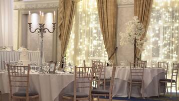 Een feestzaal met gedekte tafels, witte tafelkleden en houten stoelen.
