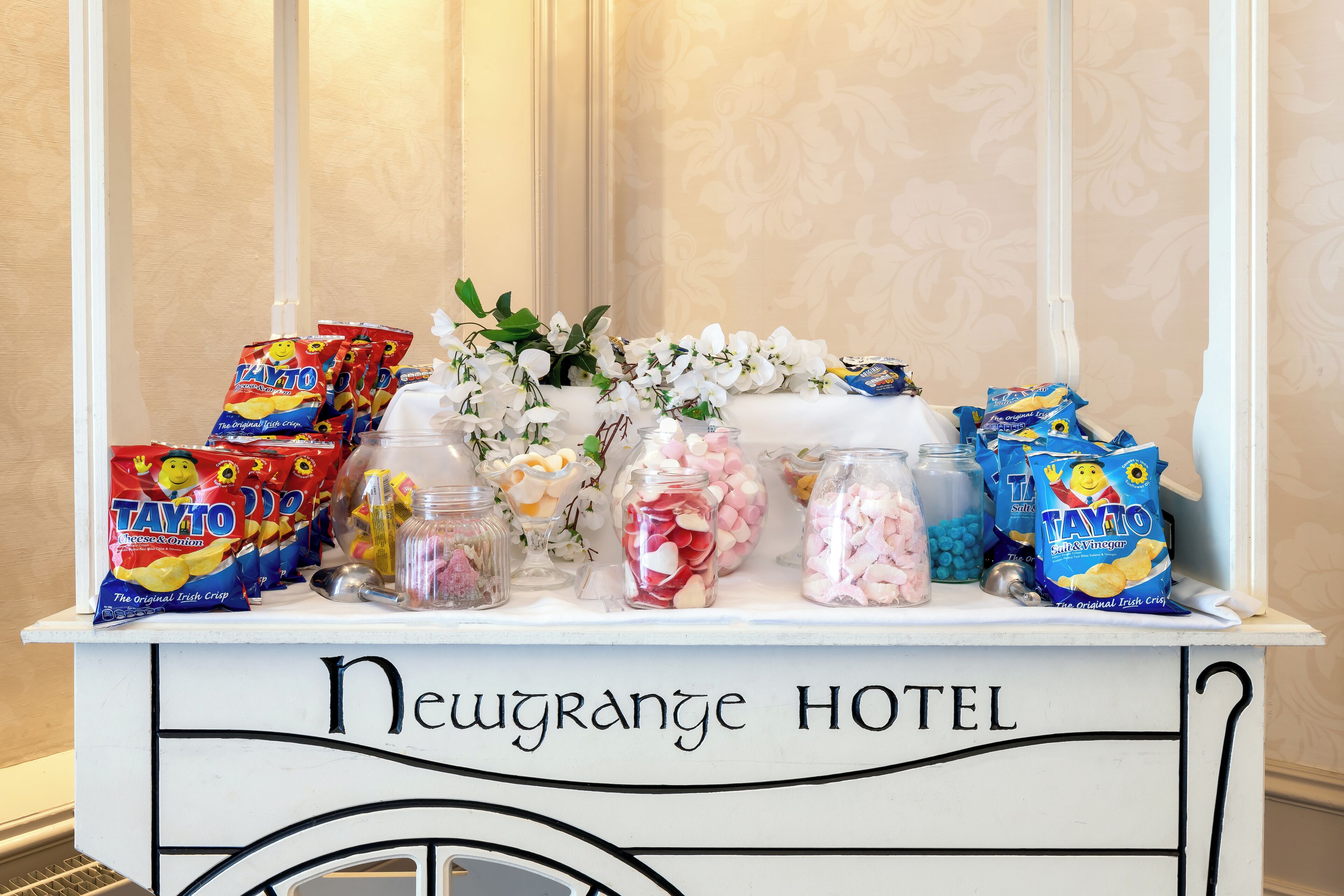 Una exhibición de bocadillos y flores sobre el mostrador de un hotel, con la leyenda 'Newgrange Hotel'.