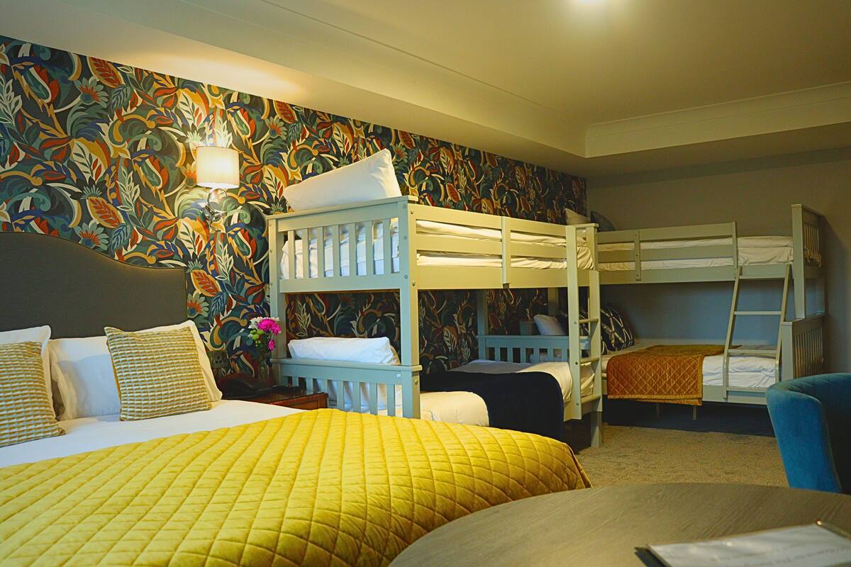 Une chambre d’hôtel avec des lits superposés, une couvre-lit jaune et un papier peint à motifs floraux.