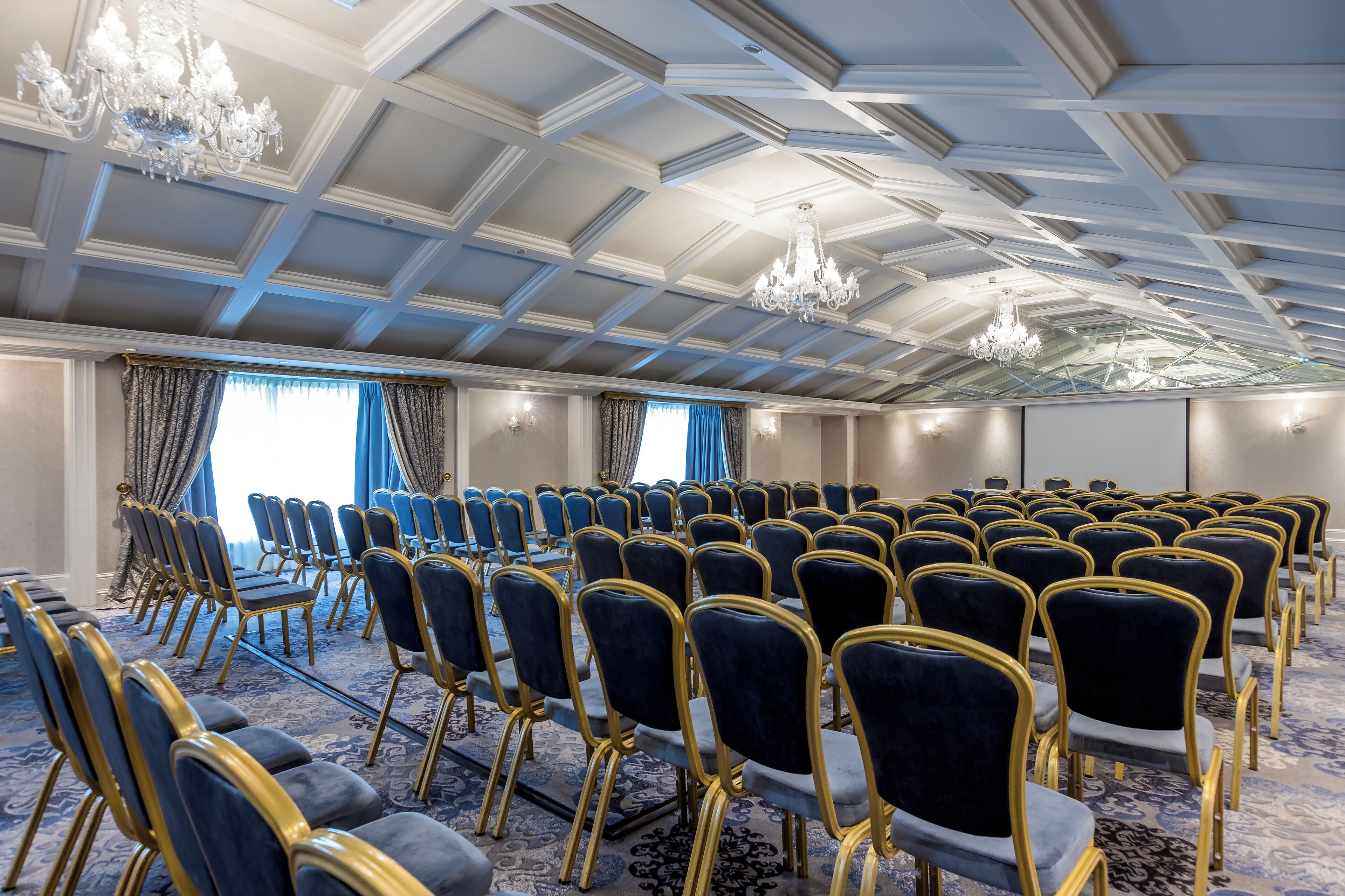 Un salón de conferencias con filas de sillas, una araña de cristal y una alfombra estampada.