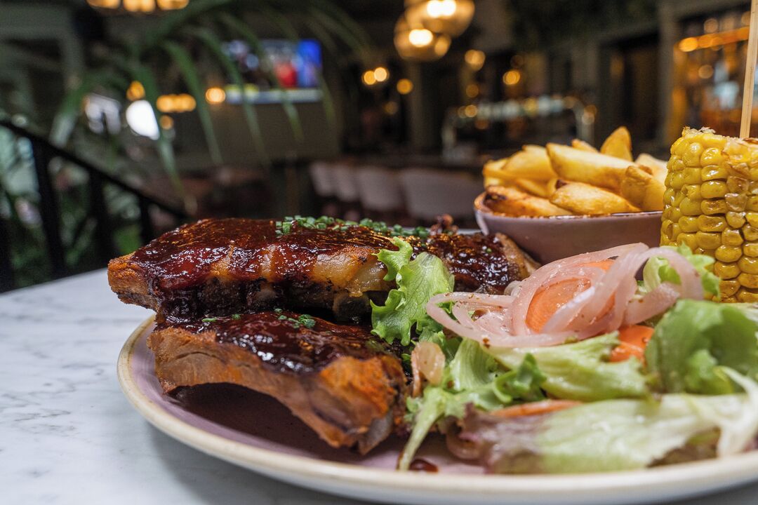 Un plato de costillas con ensalada y mazorca de maíz.