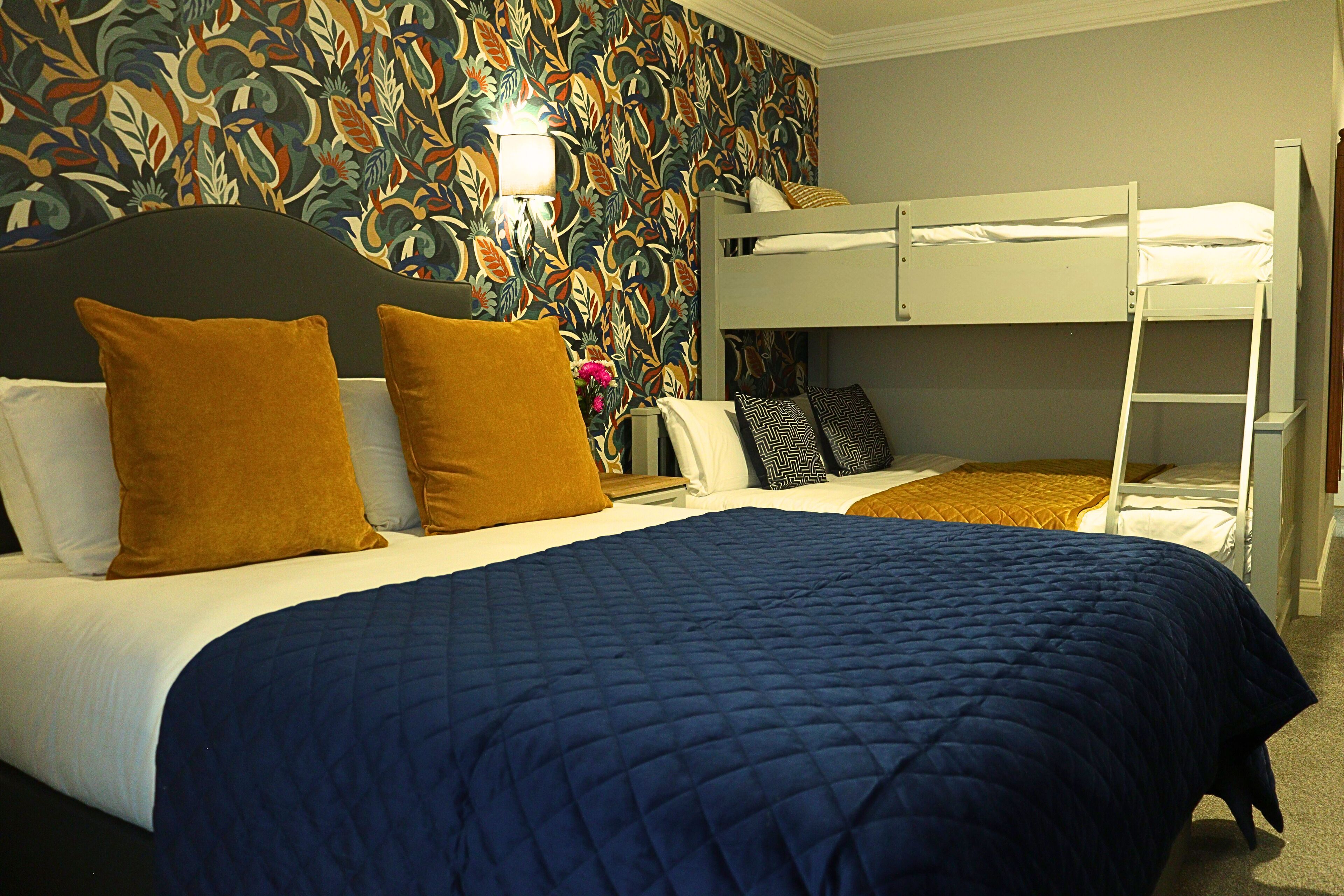 Habitación de hotel con literas, una colcha azul acolchada y un diseño de papel tapiz floral.