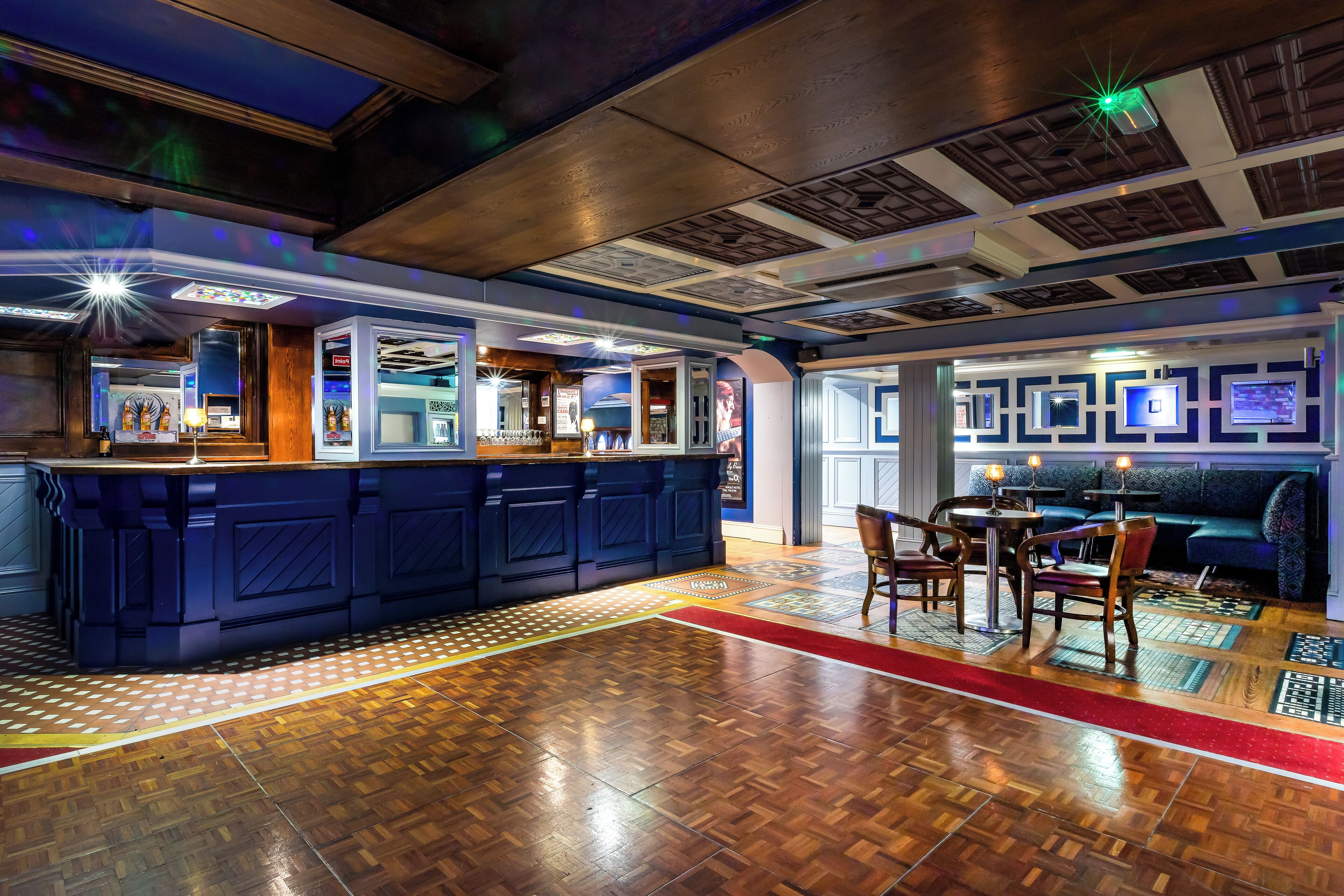 A bar area with a wooden floor, a blue bar counter, and a seating area with a sofa and chairs.
