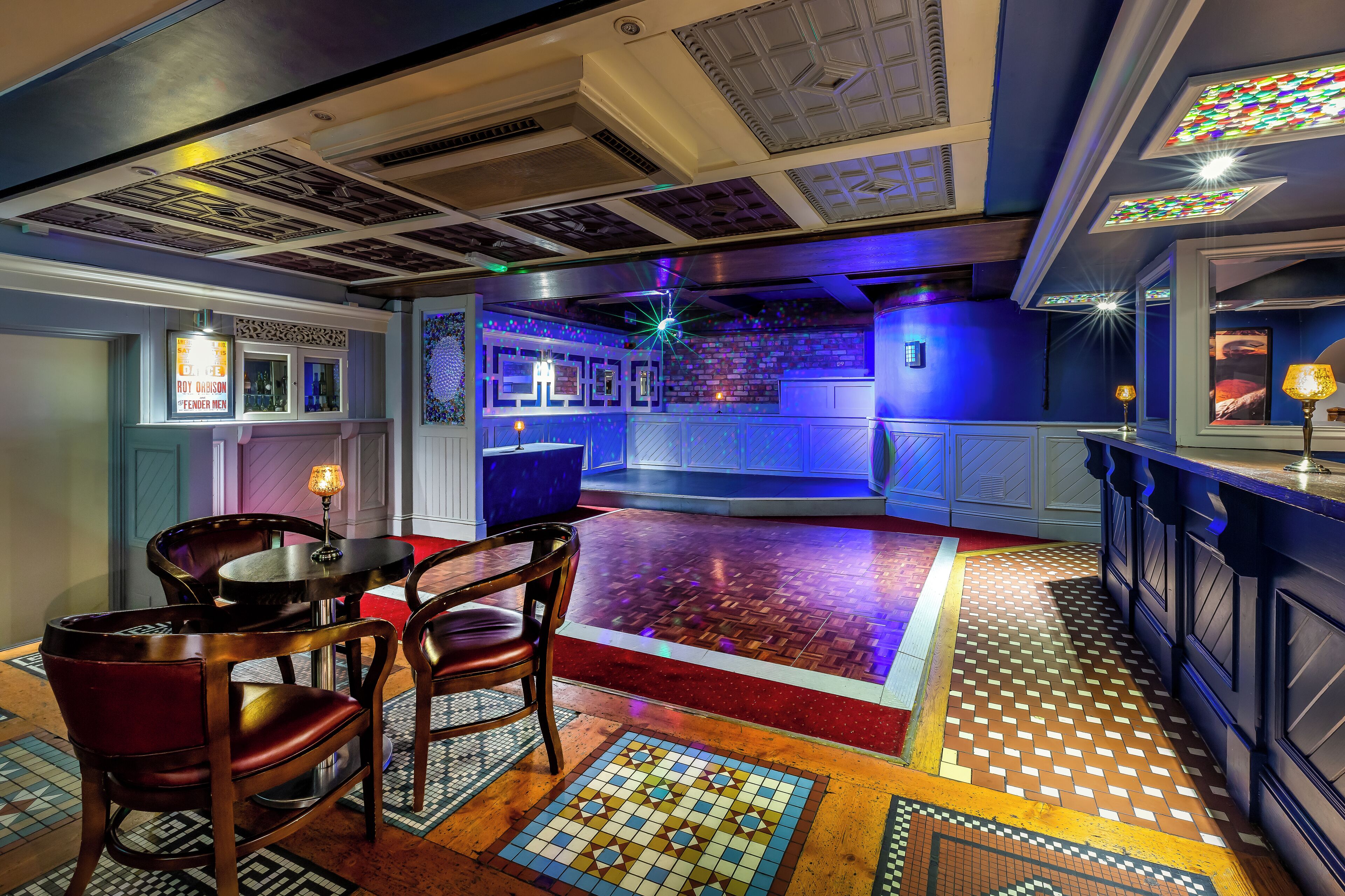 A bar area with a patterned floor, wooden chairs, and a counter.