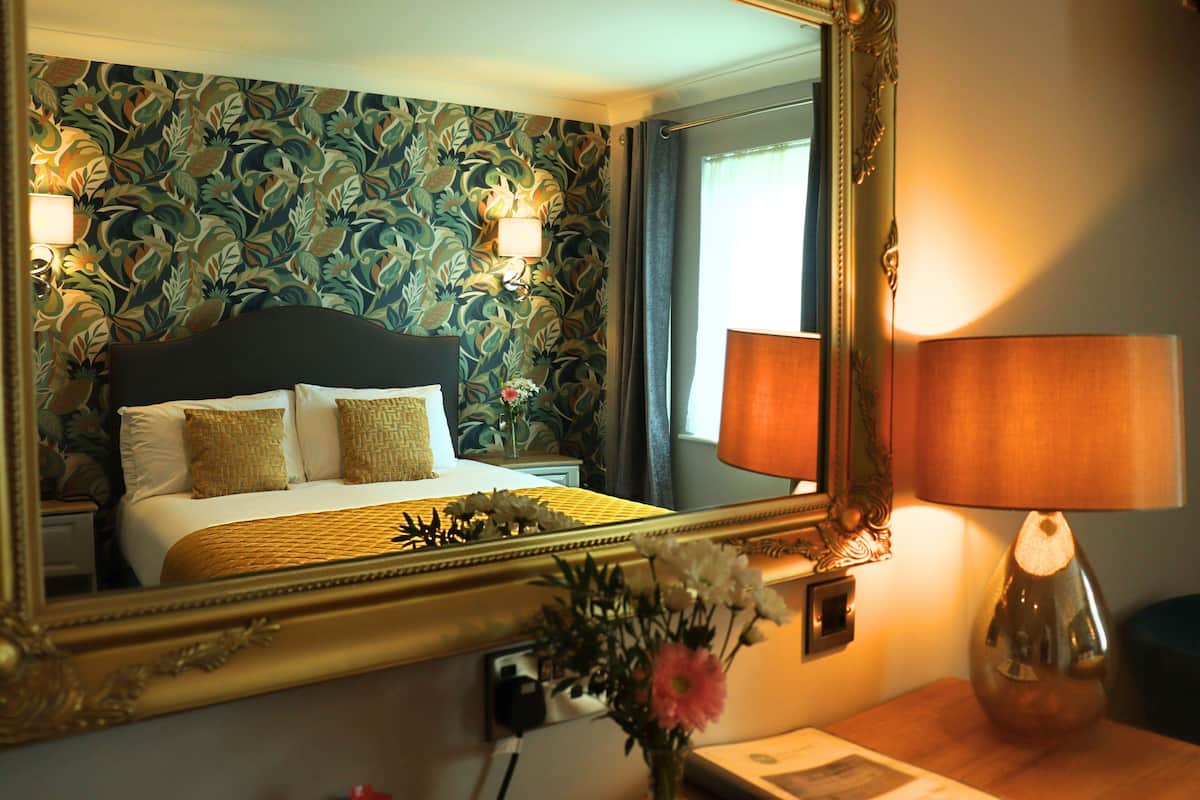 Une chambre d’hôtel avec un lit, un miroir, une lampe et un arrangement floral.