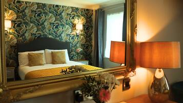 Una habitación de hotel con una cama, un espejo, una lámpara y un arreglo floral.