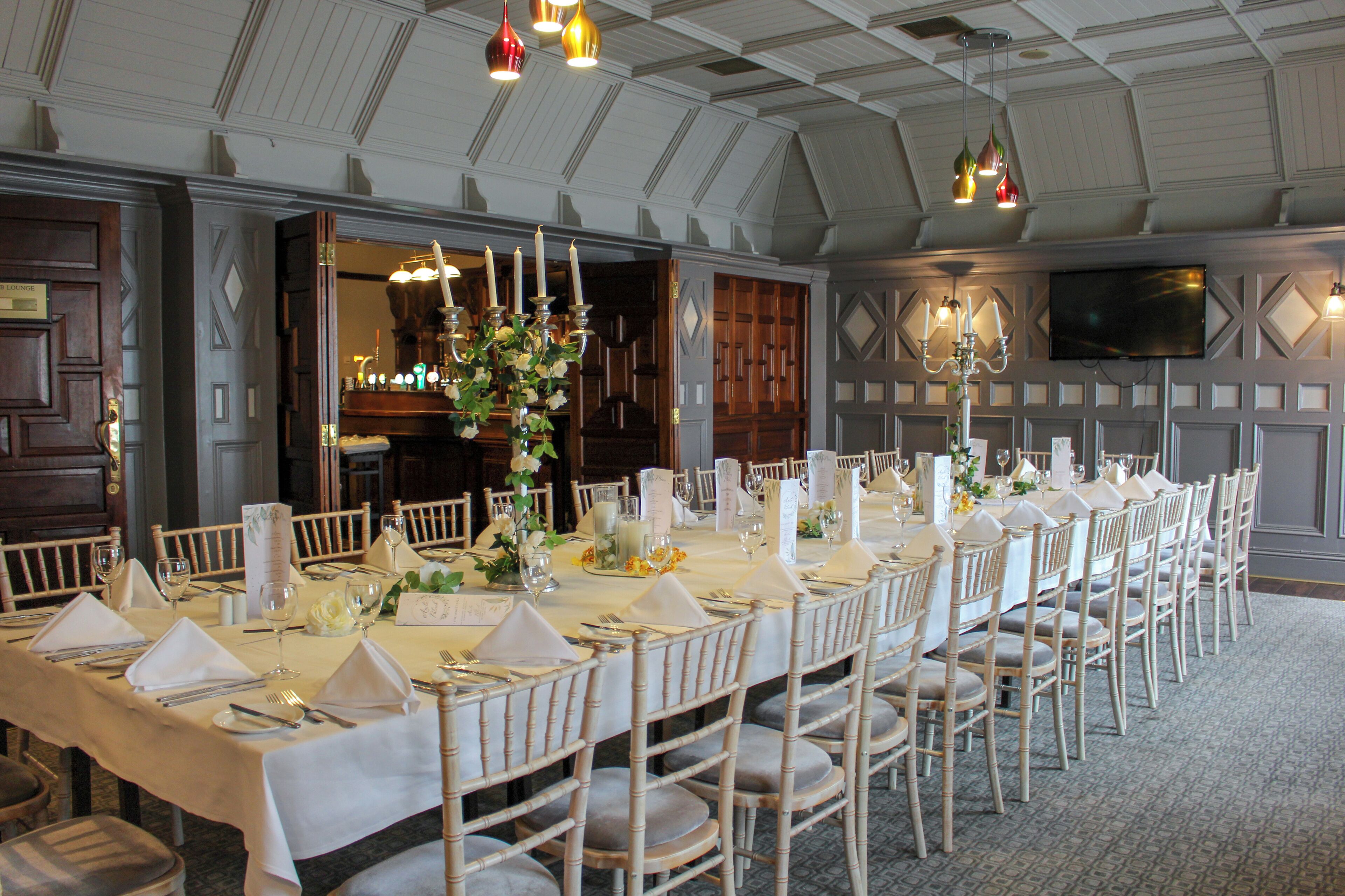 Un comedor formal con una larga mesa dispuesta para un banquete, con manteles blancos, sillas ordenadas y centros de mesa con velas.