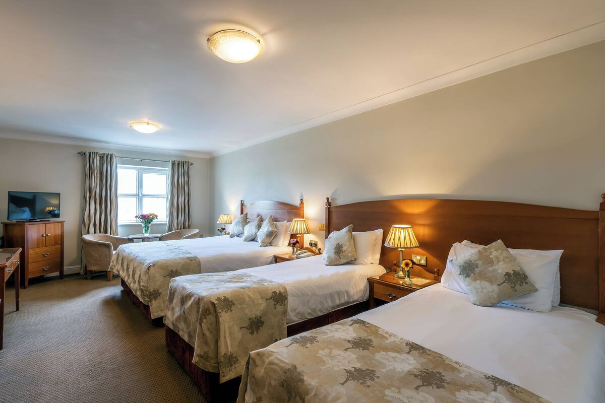 Une chambre d’hôtel avec trois lits, un bureau, une télévision et une fenêtre avec des rideaux.