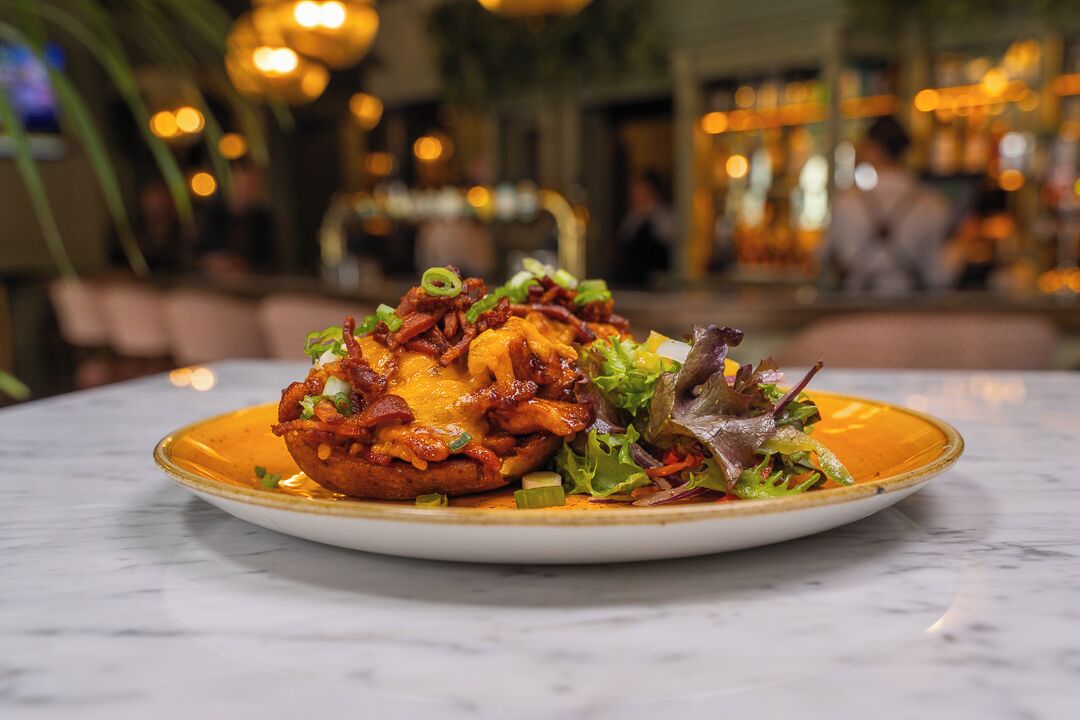 A plate of food with a crispy, golden-brown base topped with melted cheese and green onions, served on a white plate with a gold rim.