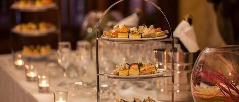 Un soporte escalonado para postres con varias capas de pastelería, un florero de cristal con flores rojas y velas sobre una mesa.