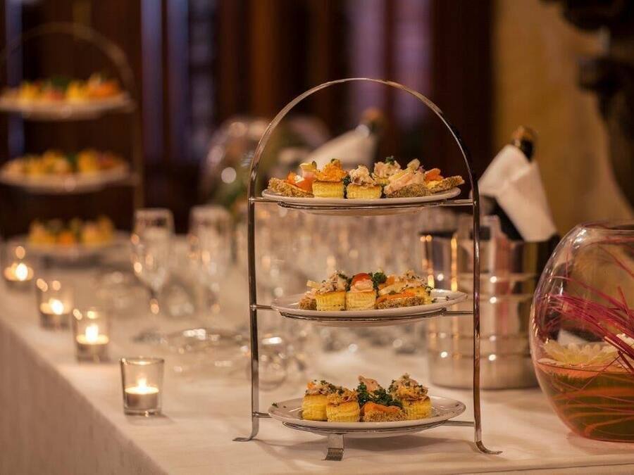 A tiered dessert stand with multiple layers of pastries, a glass vase with red flowers, and candles on a table.