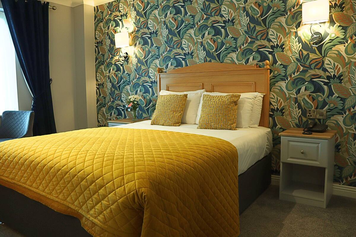 Une chambre d’hôtel avec un lit, une table de chevet et un mur orné d’un motif floral.
