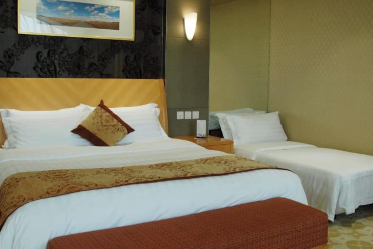 A hotel room with two beds, a headboard, a nightstand, and a wall-mounted lamp.