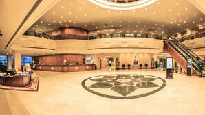 A spacious lobby with a central circular floor design, a reception desk, and an escalator. - Dalian East Hotel (Dalian)