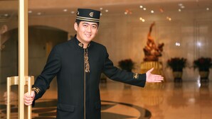 A person in a black uniform with gold embroidery, standing in a lobby with a polished floor and a statue in the background. - Dalian East Hotel (Dalian)