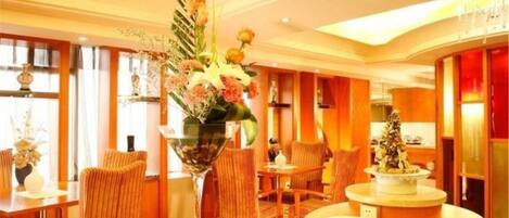 A hotel lobby with a central reception desk, seating area with chairs, and a decorative plant arrangement.