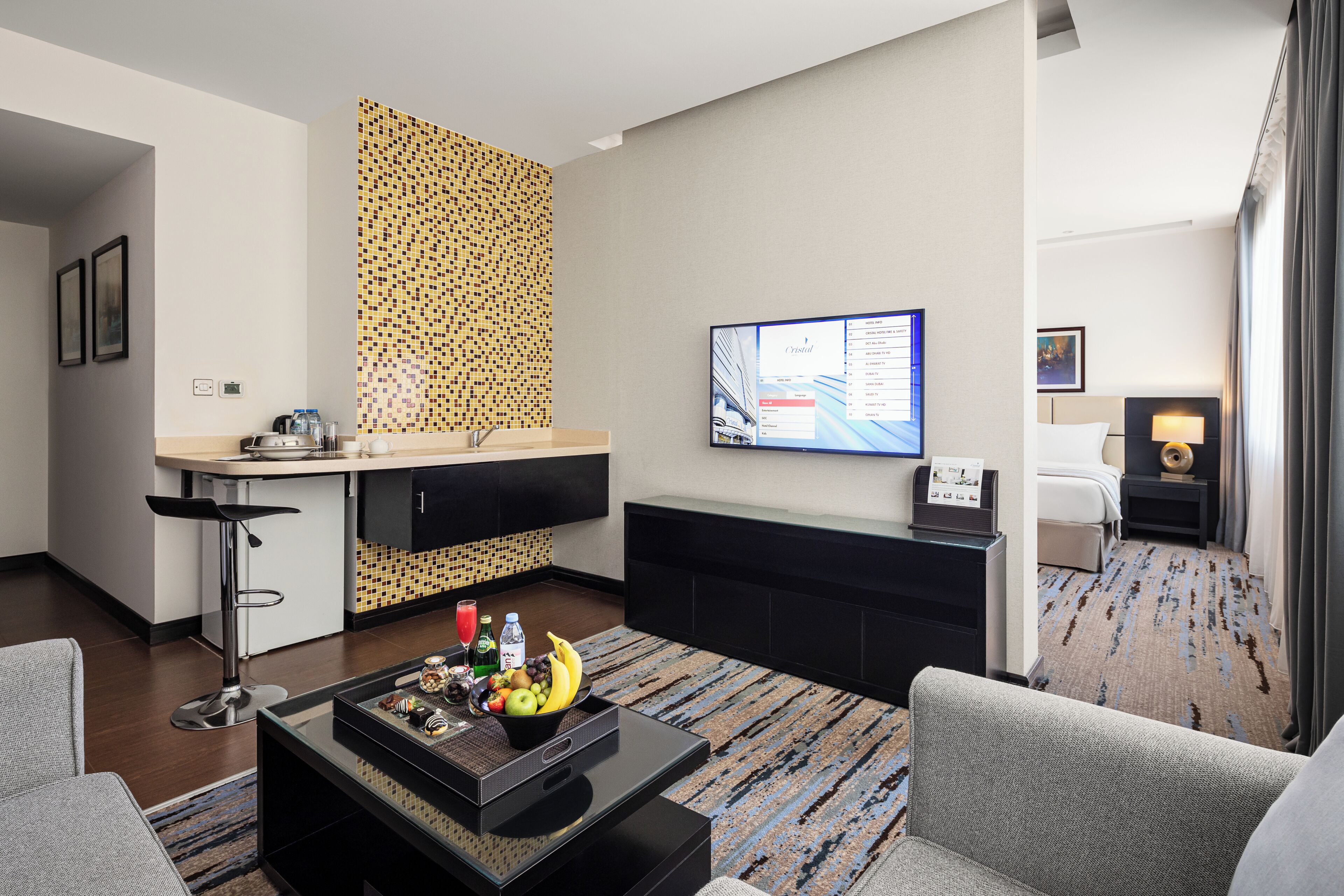 Une chambre d’hôtel moderne dotée d’un coin cuisine, d’une table à manger avec des fruits, d’une télévision et d’un canapé.