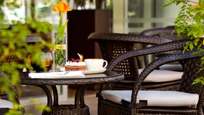 Des chaises en osier avec des coussins, une petite table ronde avec un gâteau, une tasse de café et un vase rempli de fleurs.
