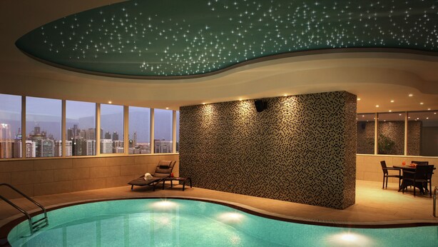 Une piscine avec vue sur la ville, un espace détente avec des fauteuils et un mur décoré de motifs.