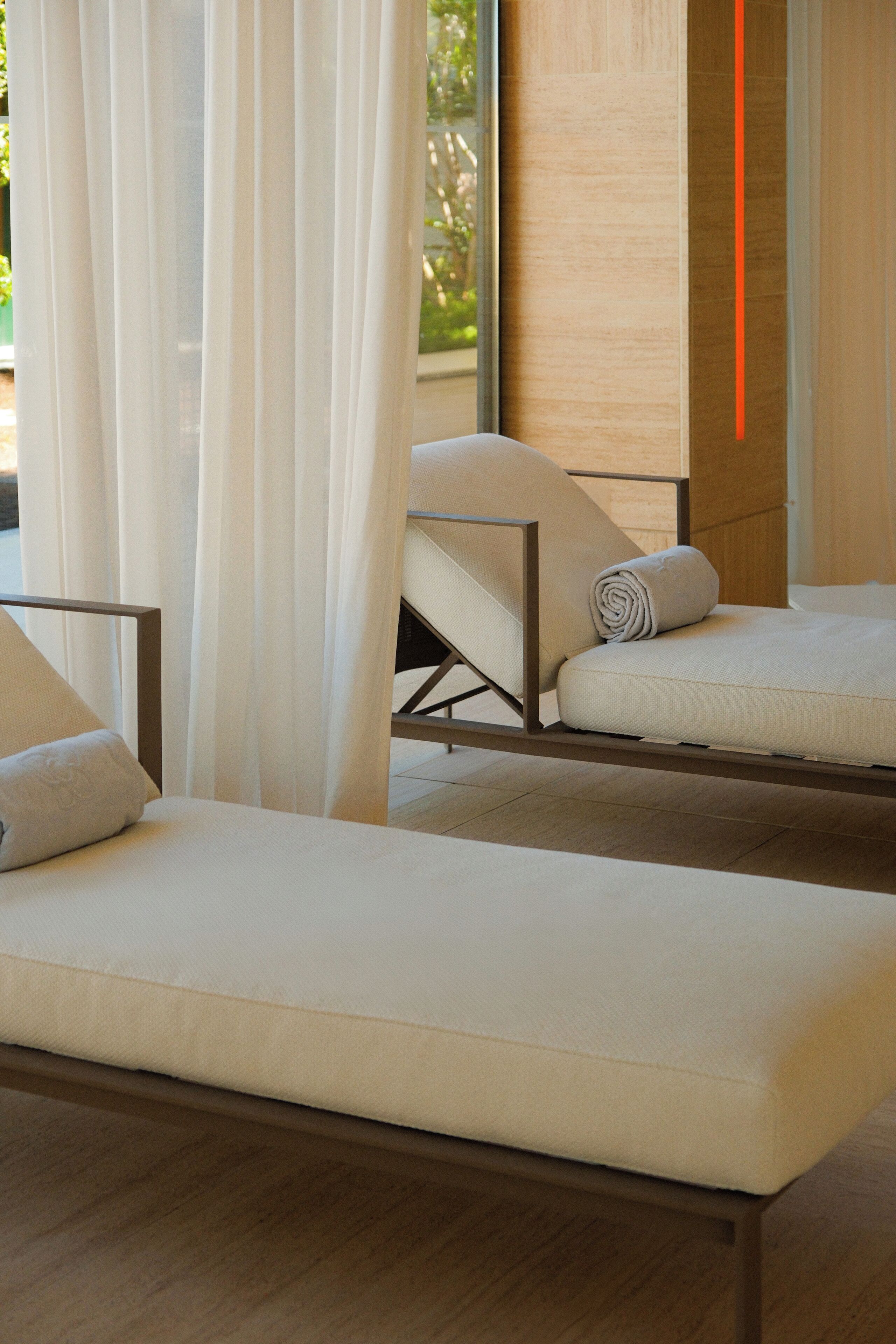 A modern room with two lounge chairs, a wooden floor, and a large window with sheer curtains.