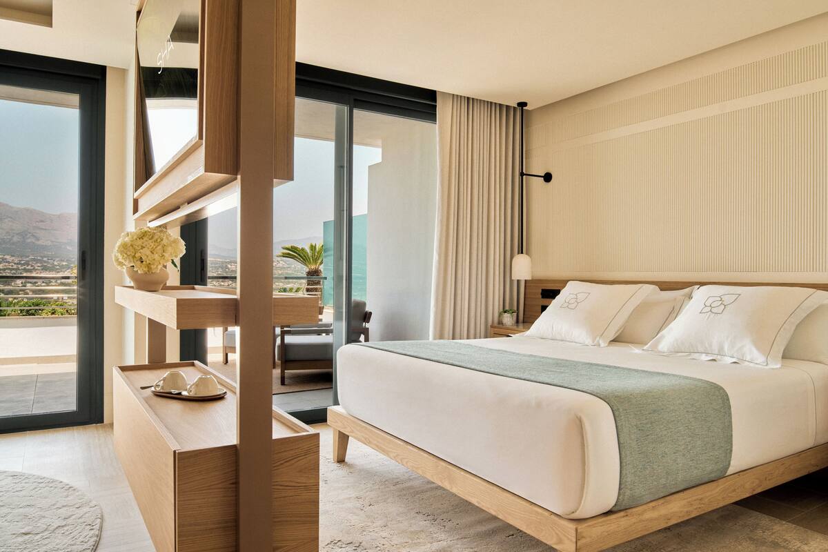Ein modernes Hotelzimmer mit einem großen Bett, einem Schreibtisch mit einer Vase und Blick auf die Stadt.
