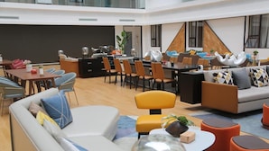 A modern hotel lobby with a mix of seating areas, including a sofa, chairs, and a dining table. There is a large window providing natural light and a view of the outdoors. - Grand Golden Phoenix (Beijing)