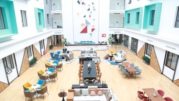 A spacious atrium with multiple seating areas, a central dining table, and a modern geometric wall design. - Grand Golden Phoenix (Beijing)