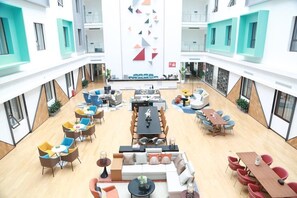 A spacious atrium with multiple seating areas, a central dining table, and a modern geometric wall design. - Grand Golden Phoenix (Beijing)