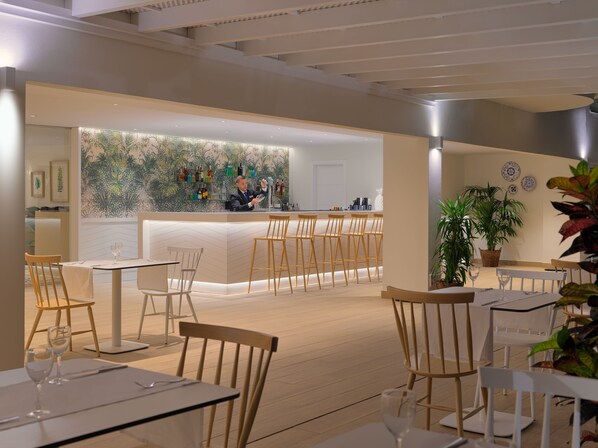 A modern restaurant interior with a bar area, wooden chairs, and tables. - H10 Ocean Dunas - Adults Only (La Oliva)