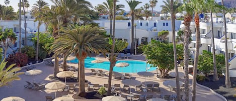 A resort with a swimming pool surrounded by palm trees and lounge chairs.