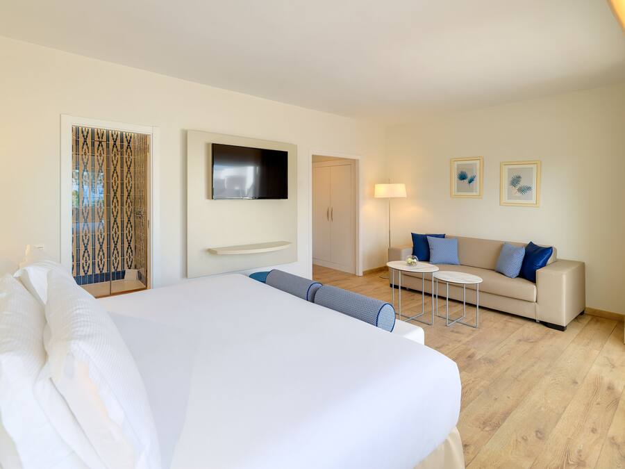A hotel room with a large bed, a TV mounted on the wall, a sofa, a small table, and two framed pictures on the wall.