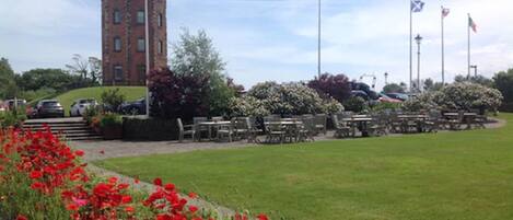 A courtyard with a brick tower, outdoor seating, and flags.