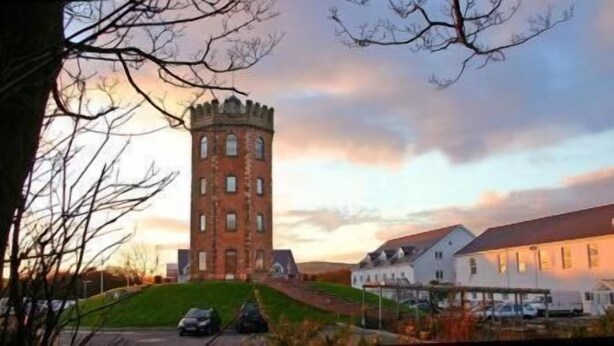 A tower with a square base and a conical roof, surrounded by buildings with white walls and red roofs. - The Towers Hotel and Spa (Neath)