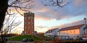 A tower with a square base and a conical roof, surrounded by buildings with white walls and red roofs. - The Towers Hotel and Spa (Neath)