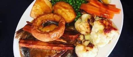 A plate of food including roast beef, Yorkshire pudding, peas, carrots, and mashed potatoes.