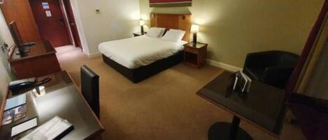 A hotel room with a bed, bedside tables, a desk, and a chair.