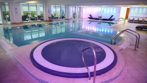 An indoor swimming pool with a hot tub, lounge chairs, and a glass-enclosed area with seating. - The Towers Hotel and Spa (Neath)