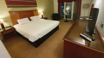 A hotel room with a large bed, a desk with a mirror, a chair, and a TV.