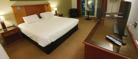 A hotel room with a large bed, a desk with a mirror, a chair, and a TV.