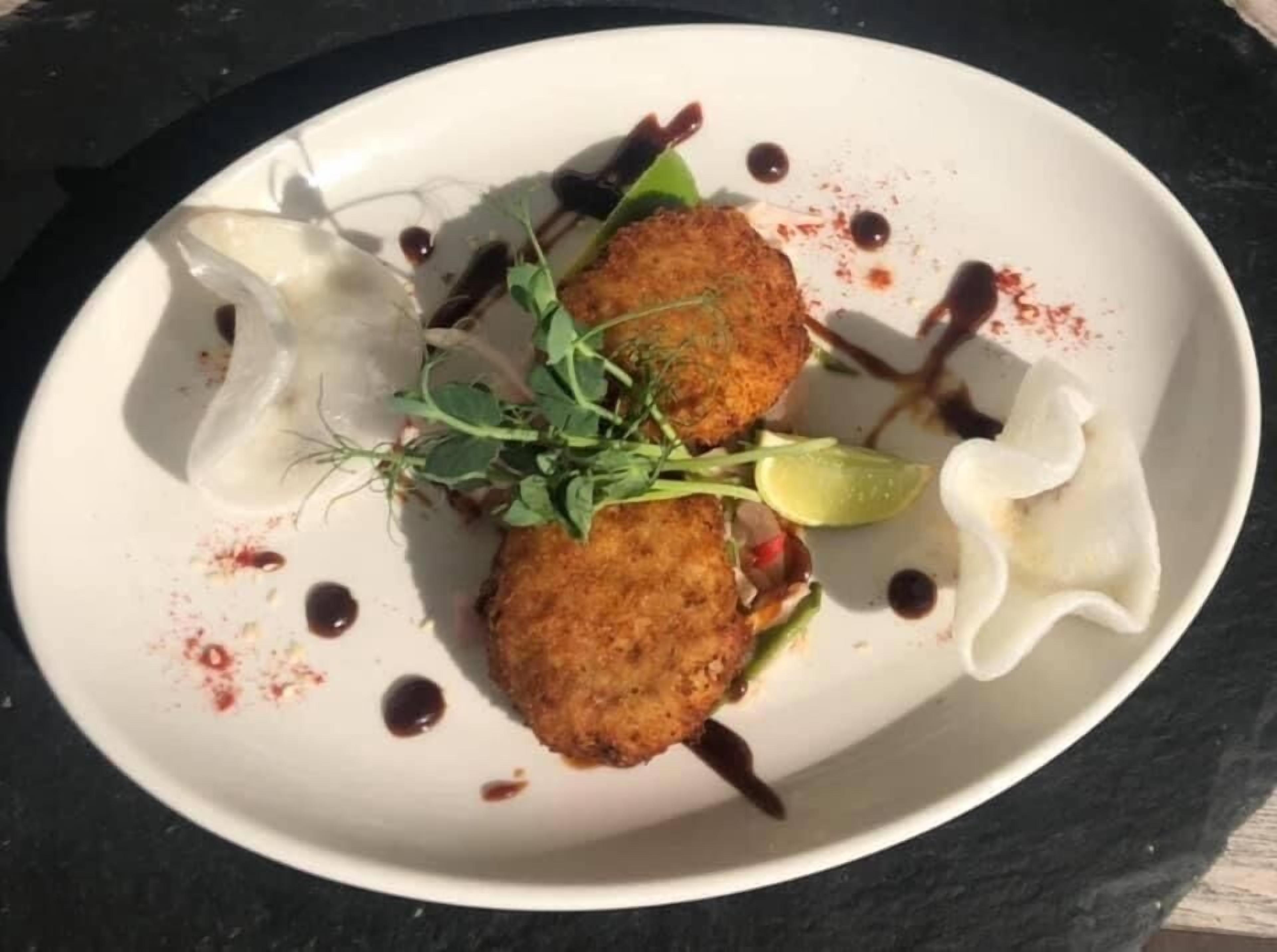 A white plate with two fried items, garnished with green leaves and a lime wedge, on a dark surface.