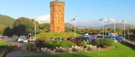 A tower with a flag, surrounded by a parking area and greenery.