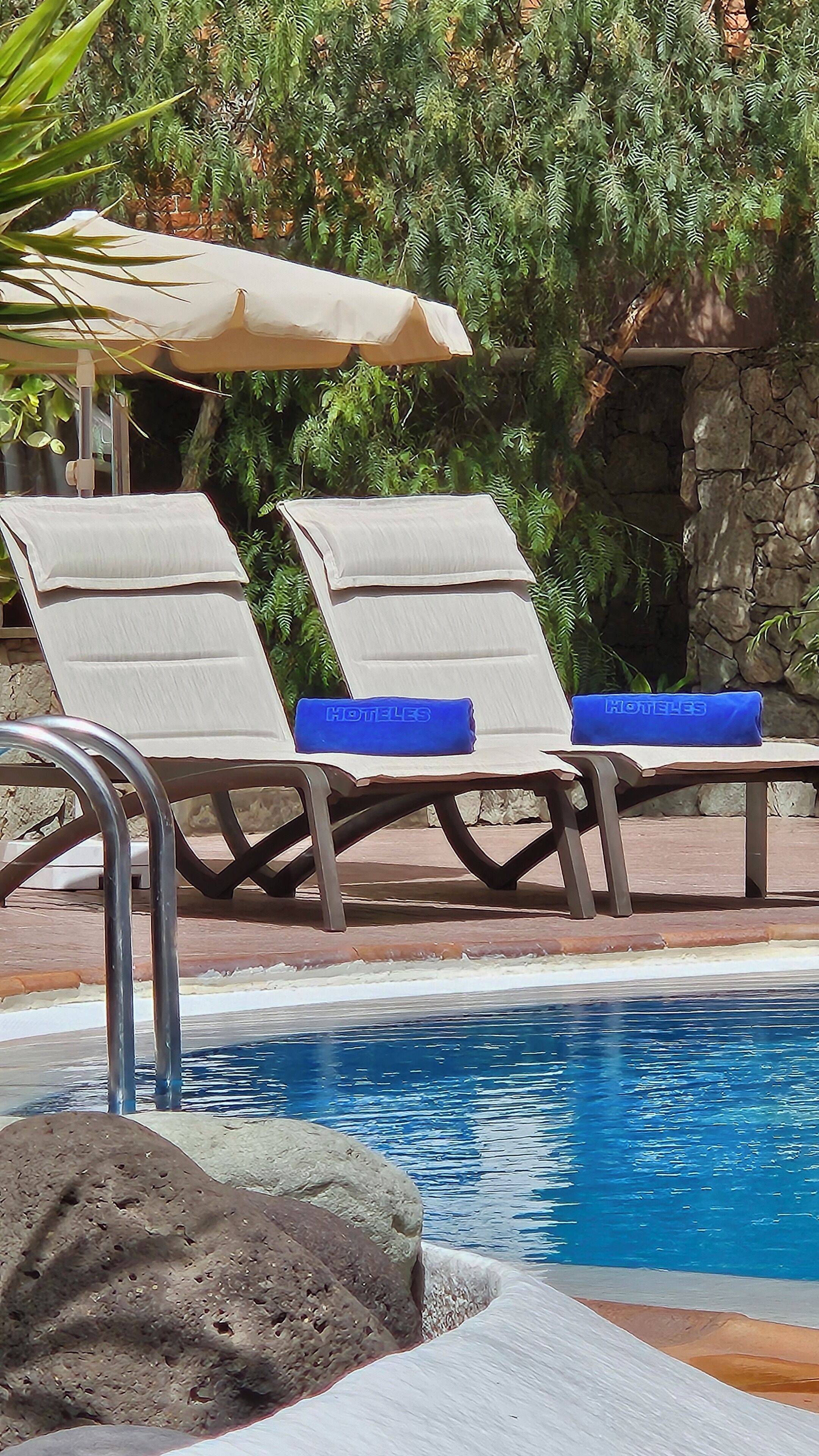 Un área junto a la piscina con sillones de descanso y una pared de piedra.