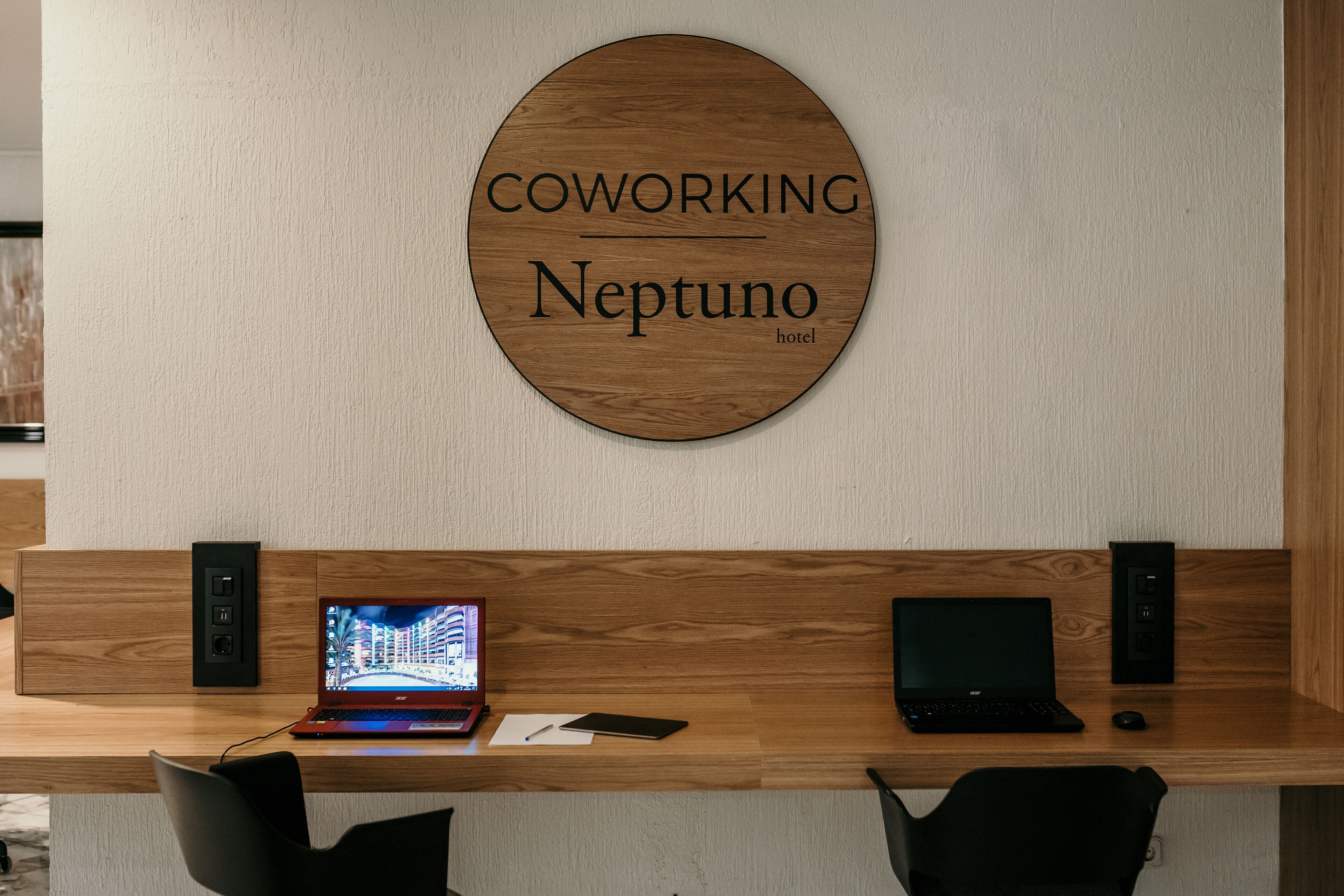 A coworking space with a wooden desk, two laptops, a tablet, and a smartphone.