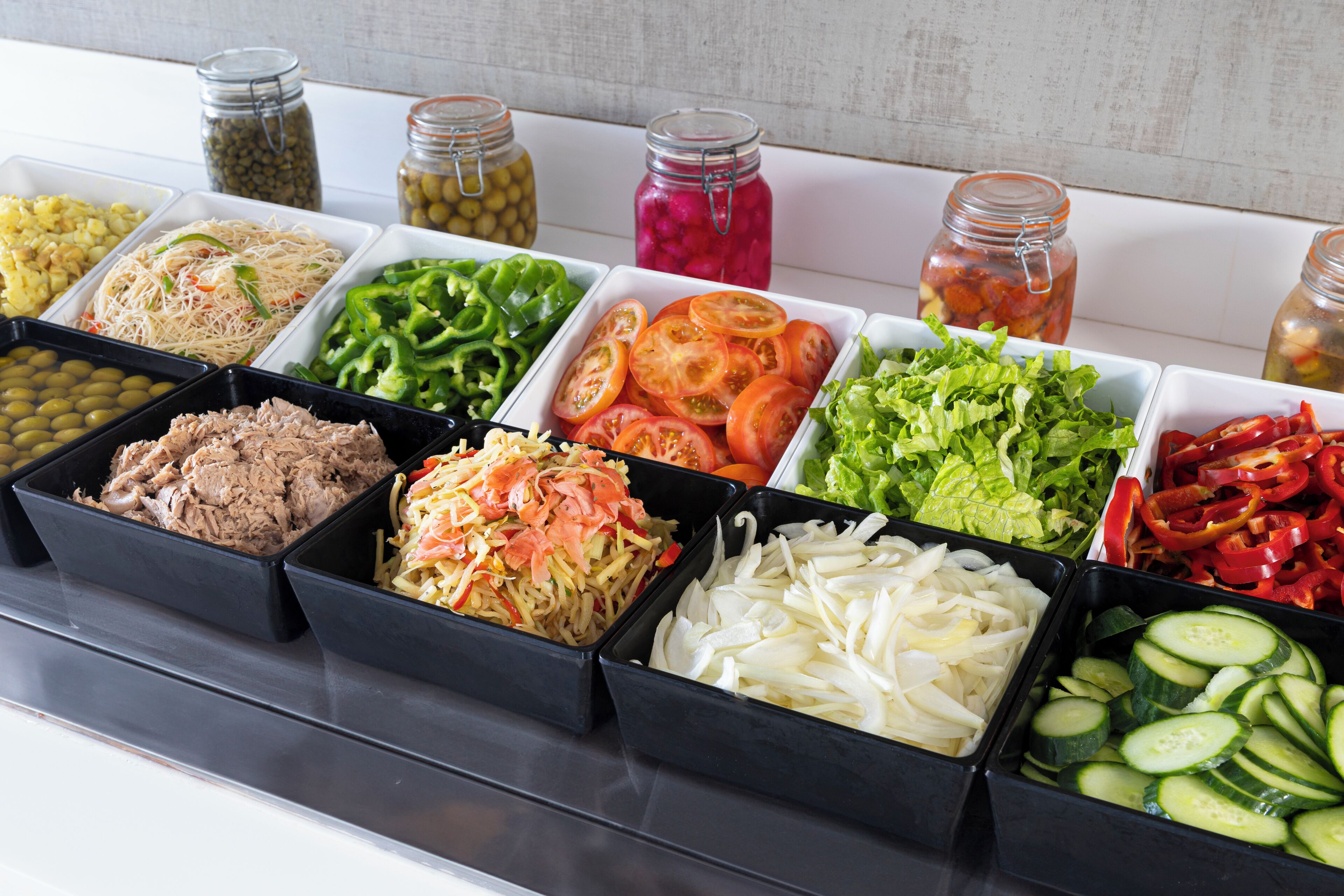 A variety of food items in black containers, including vegetables, salads, and pickled items.