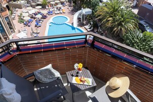 Un balcón con vistas a una piscina, sillas de descanso y una mesa con comida y un sombrero.