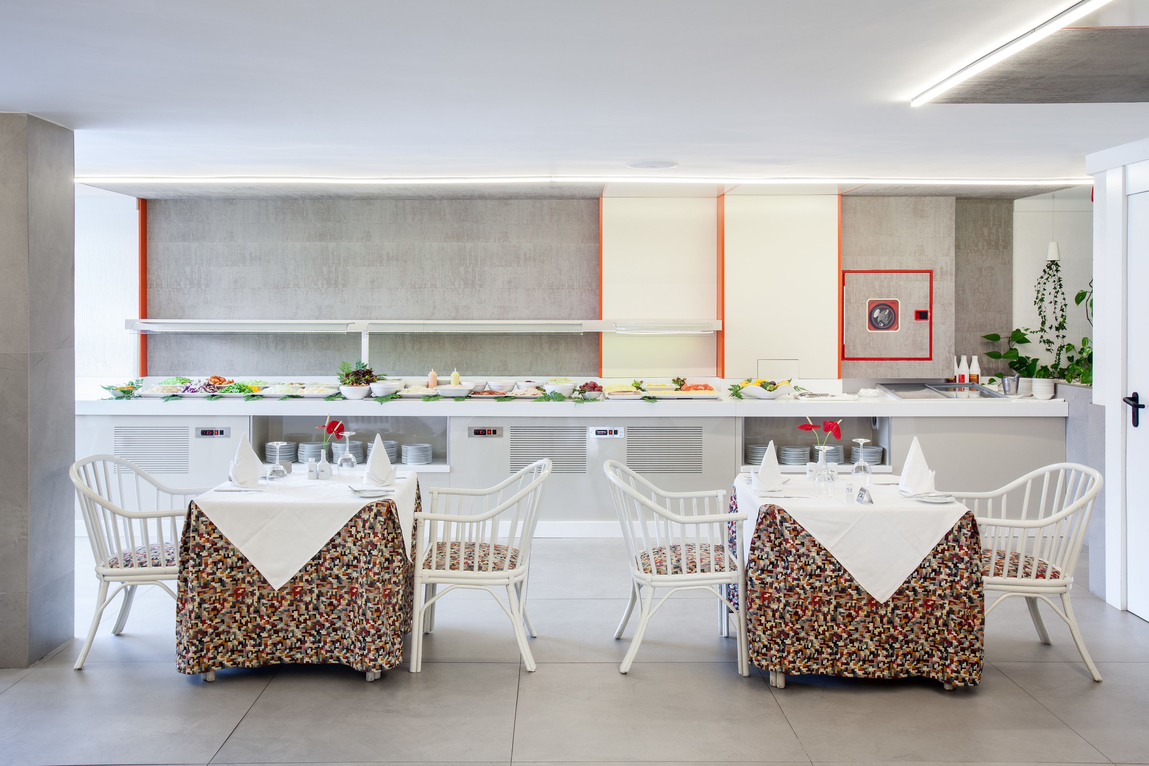 A modern dining area with a long counter, white chairs, and a buffet setup.