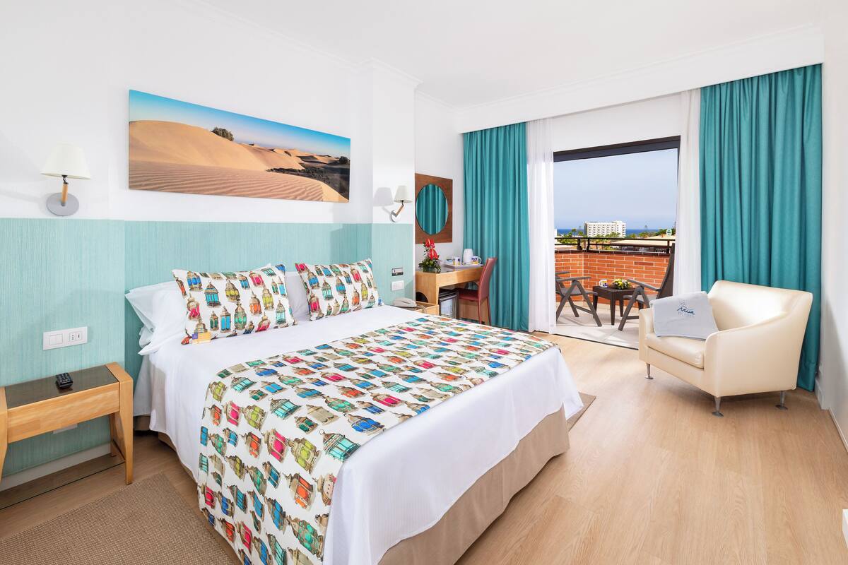 Une chambre d’hôtel avec un grand lit, un bureau, une chaise et un balcon avec vue.