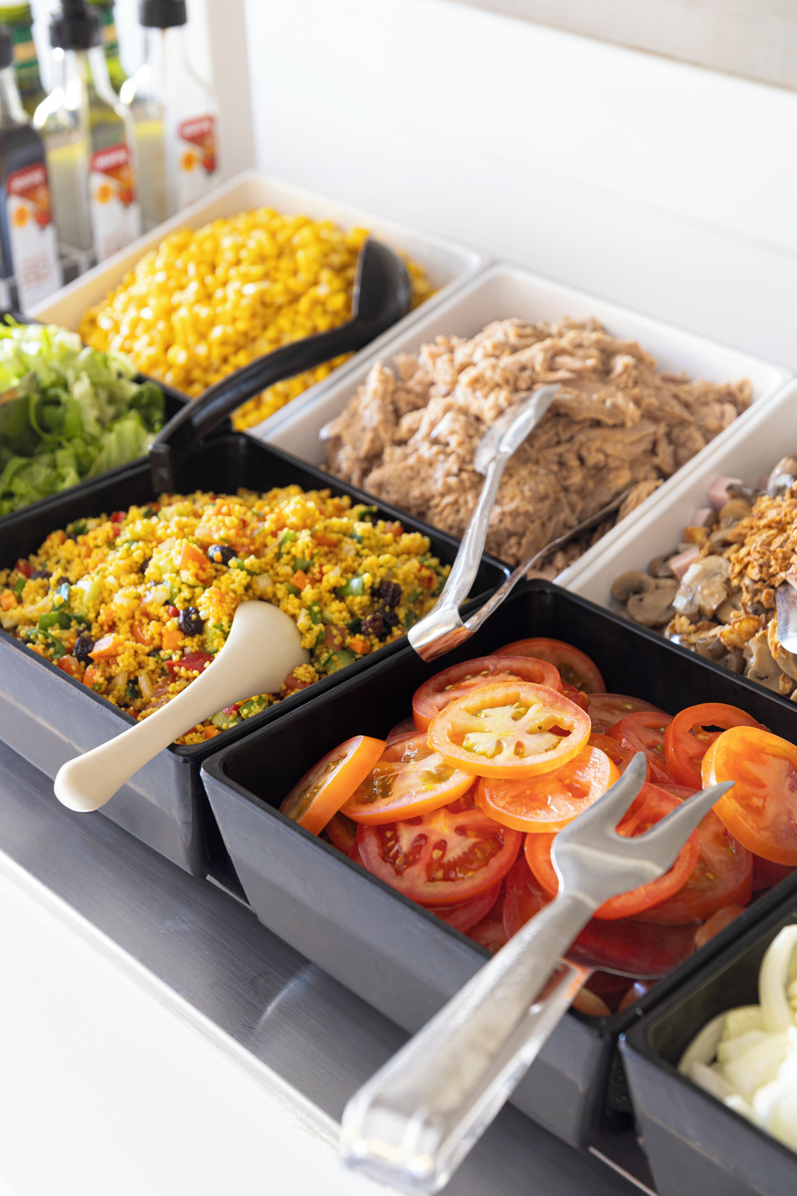 A buffet with various food options including corn, rice, and sliced tomatoes.